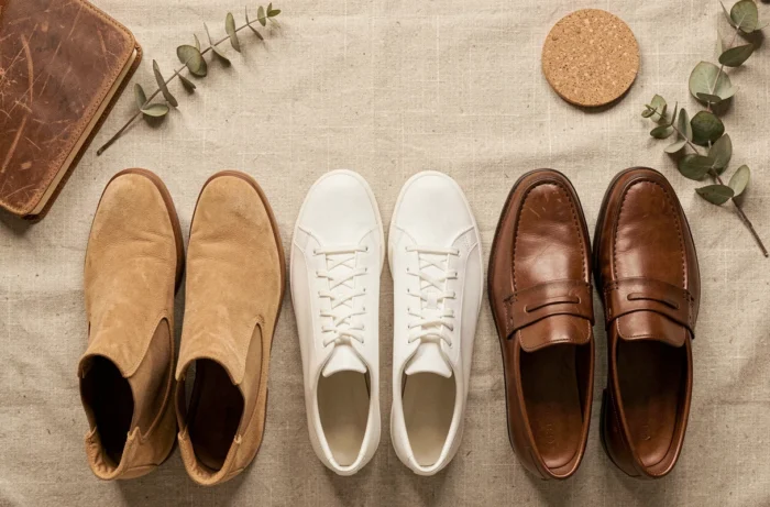 Flat-lay de trois paires de chaussures en cuir et daim sur lin naturel, illustrant diversité de styles, durabilité et confort au quotidien